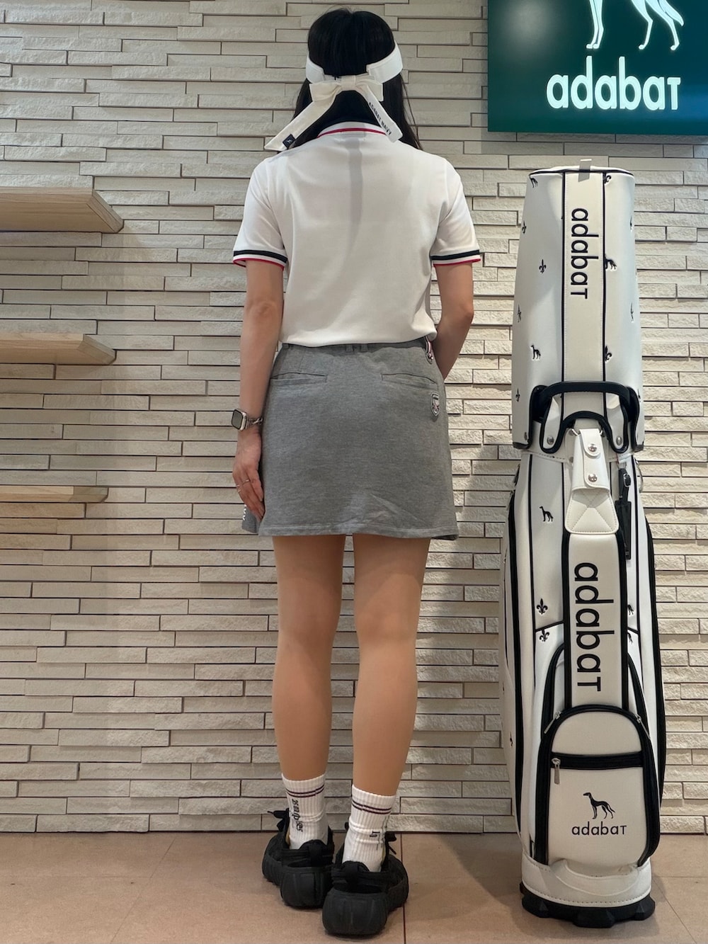 ホワイト系のポロシャツ、グレー系のスカート、ホワイト系のサンバイザーを着用したレディースの夏コーディネートの3枚目の写真