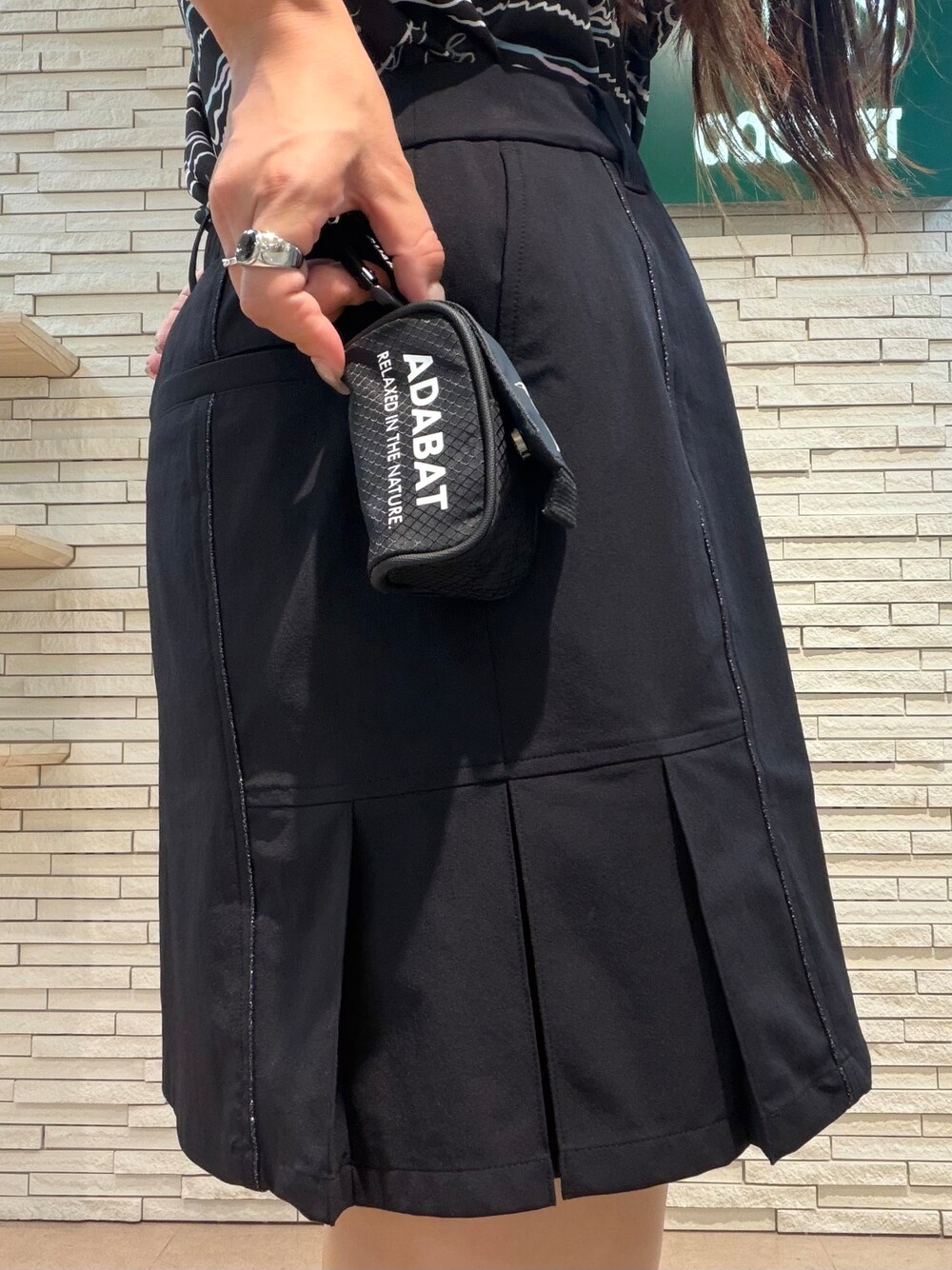 ブラック系のポロシャツ、ブラック系のスカート、ホワイト系のサンバイザーを着用したレディースの夏コーディネートの5枚目の写真