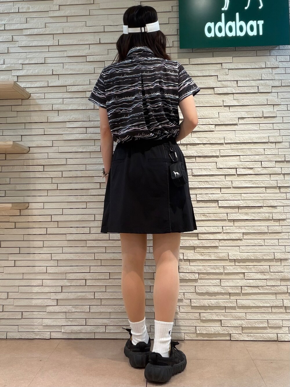 ブラック系のポロシャツ、ブラック系のスカート、ホワイト系のサンバイザーを着用したレディースの夏コーディネートの3枚目の写真