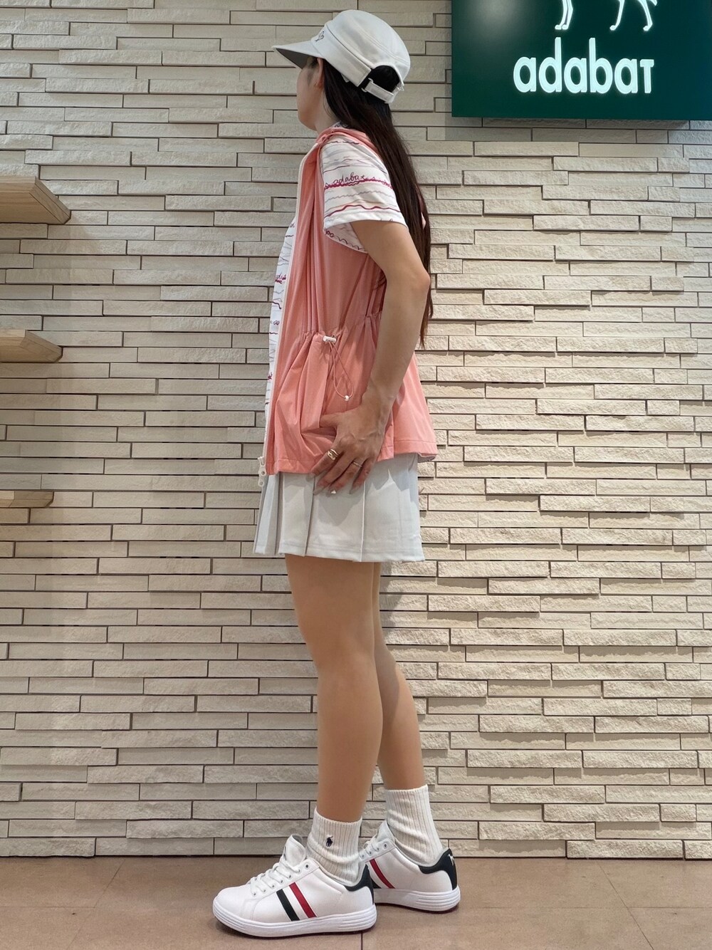 ピンク系のポロシャツ、グレー系のスカート、ピンク系のベストを着用したレディースの夏コーディネートの2枚目の写真