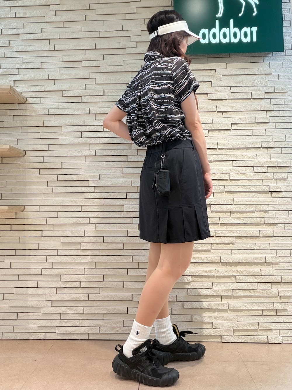 ブラック系のポロシャツ、ブラック系のスカート、ホワイト系のサンバイザーを着用したレディースの夏コーディネートの2枚目の写真