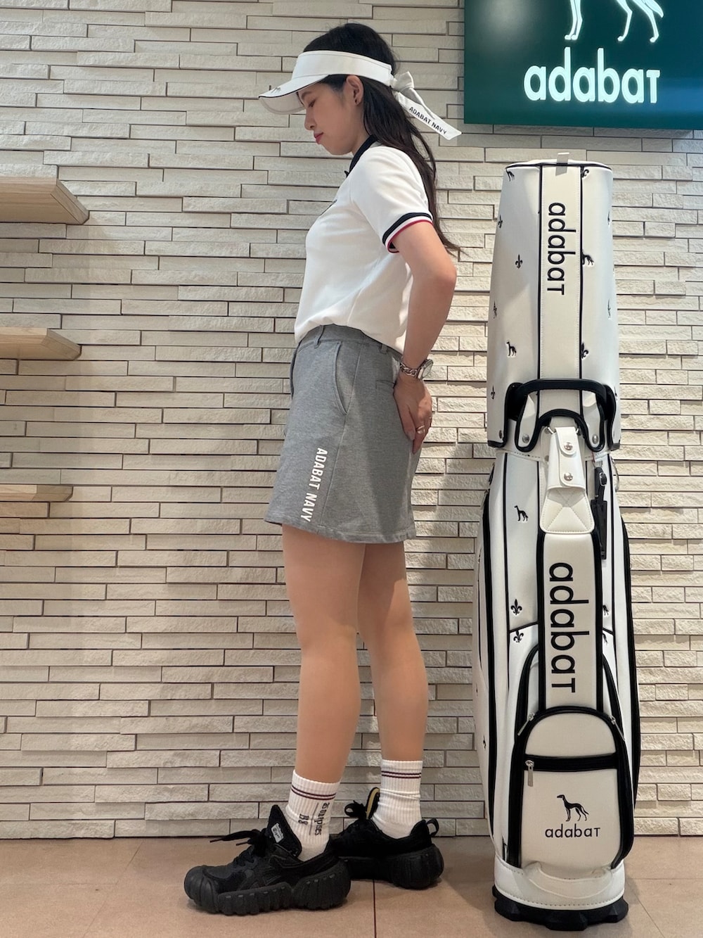 ホワイト系のポロシャツ、グレー系のスカート、ホワイト系のサンバイザーを着用したレディースの夏コーディネートの2枚目の写真