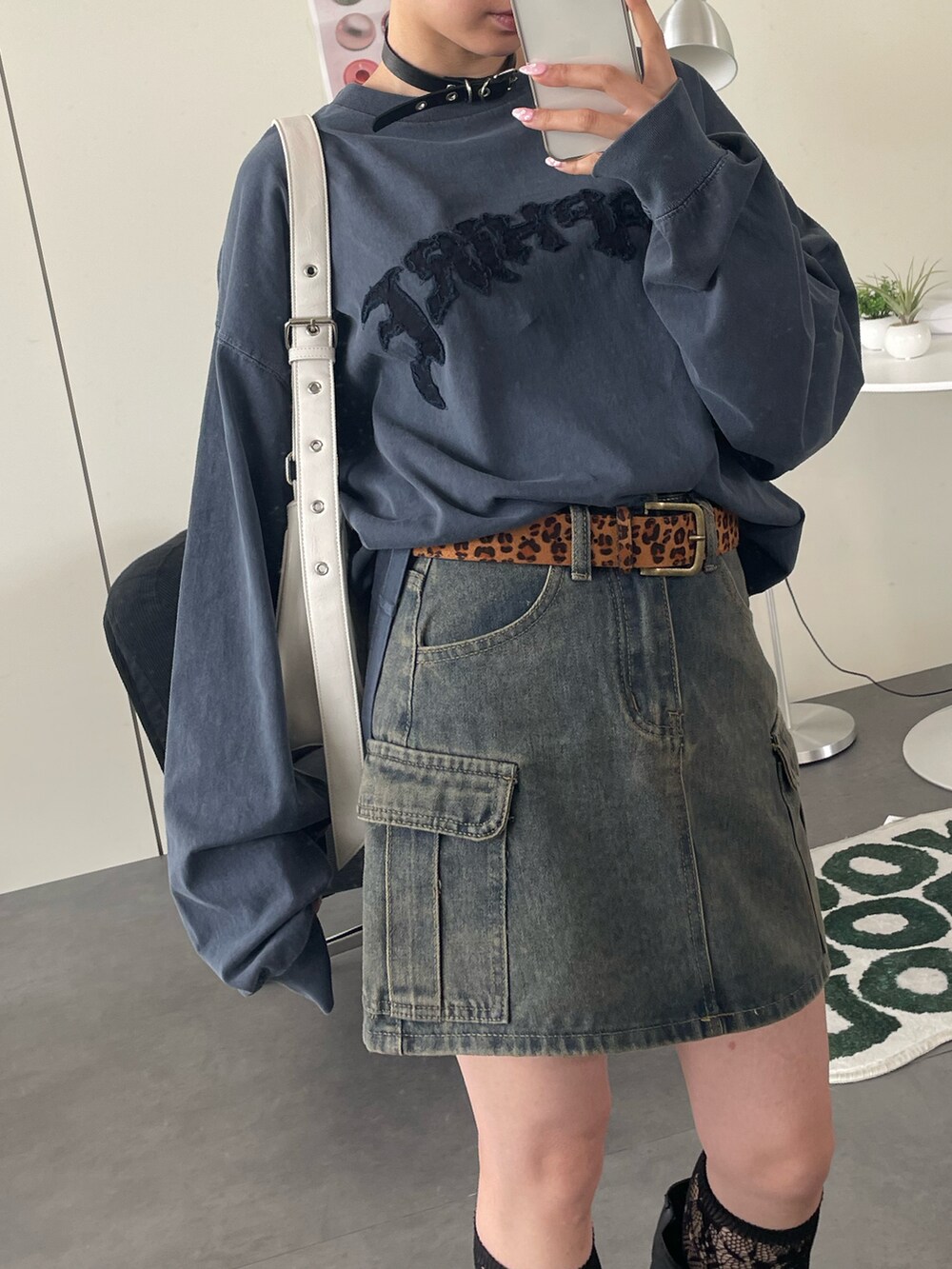 ブラック系のブーツ、ブルー系のデニムスカート、ホワイト系のショルダーバッグを着用したレディースの秋コーディネートの2枚目の写真