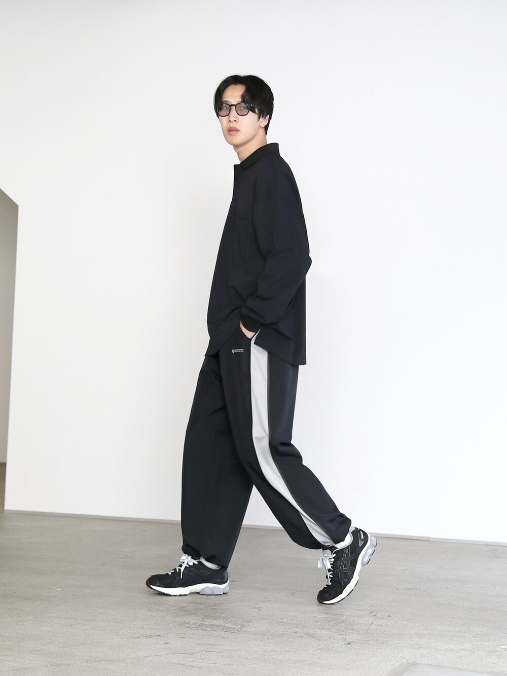 ブラック系のポロシャツ、ブラック系のパンツ、ブラック系のスニーカーを着用したメンズの春コーディネートの2枚目の写真