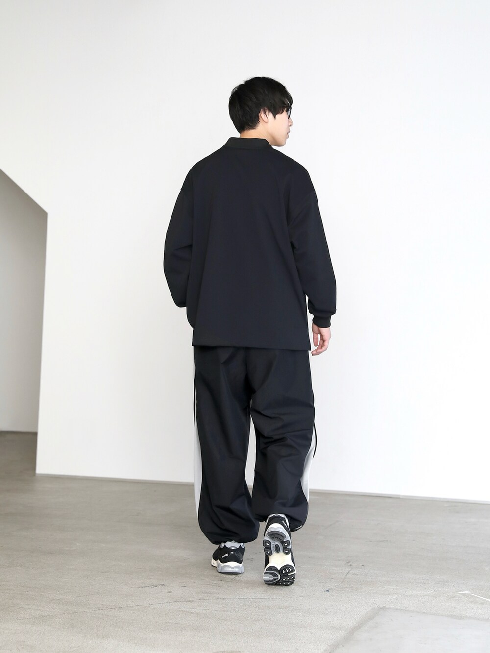 ブラック系のポロシャツ、ブラック系のパンツ、ブラック系のスニーカーを着用したメンズの春コーディネートの3枚目の写真