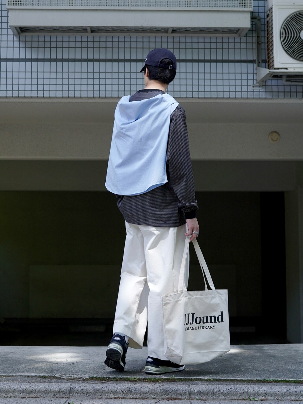 ホワイト系のチノパンツ、ホワイト系のトートバッグ、ブルー系のスニーカーを着用したメンズの春コーディネートの2枚目の写真