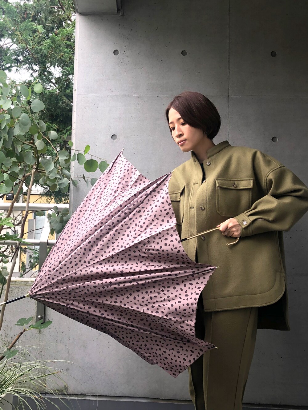 グリーン系のジャケット/アウター、ブラウン系の長傘を着用したレディースの秋コーディネートの2枚目の写真