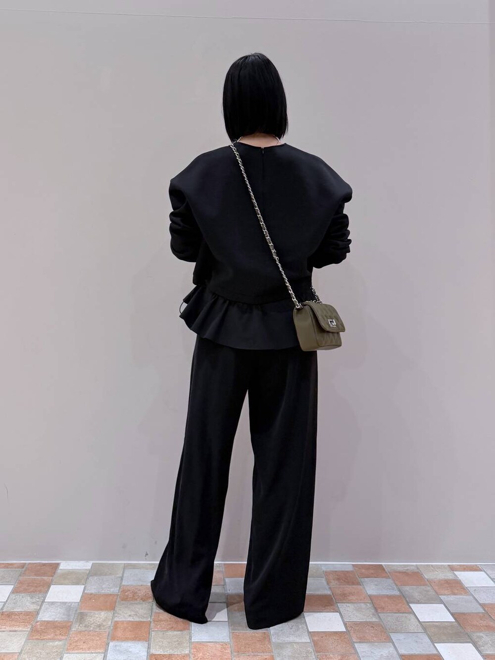 ブラック系のスラックス、ブラック系のTシャツ/カットソー、グリーン系のショルダーバッグを着用したレディースの冬コーディネートの3枚目の写真