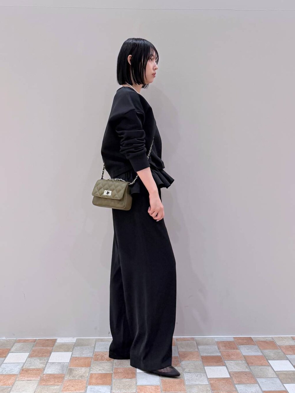 ブラック系のスラックス、ブラック系のTシャツ/カットソー、グリーン系のショルダーバッグを着用したレディースの冬コーディネートの2枚目の写真