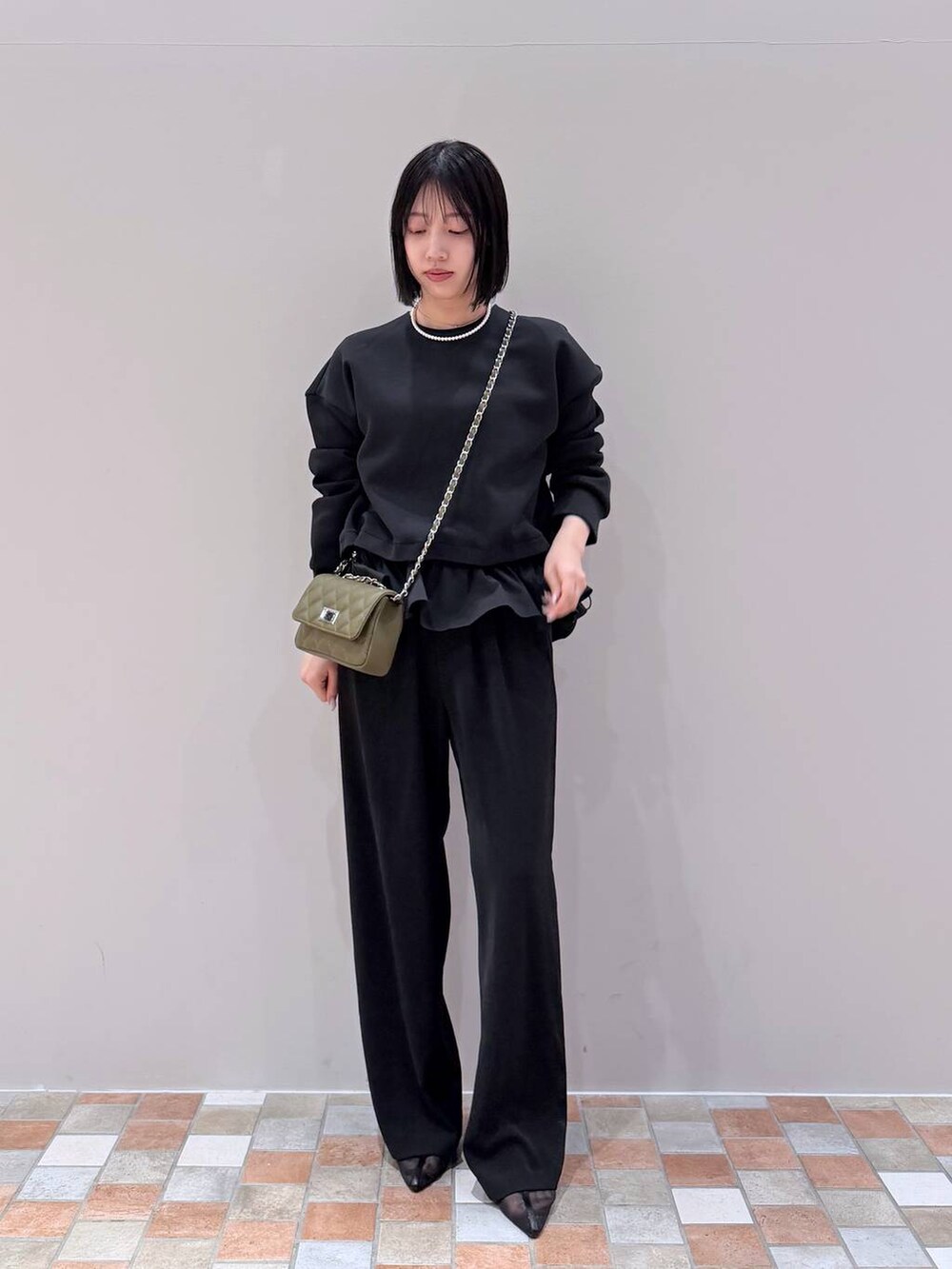 ブラック系のスラックス、ブラック系のTシャツ/カットソー、グリーン系のショルダーバッグを着用したレディースの冬コーディネートの4枚目の写真