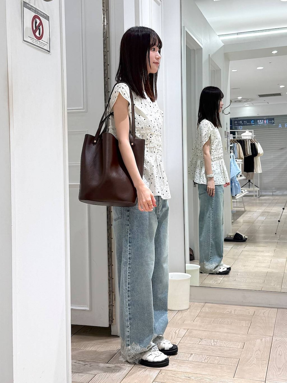 ブルー系のデニムパンツ、ホワイト系のサンダル、ブラウン系のトートバッグを着用したレディースの夏コーディネートの2枚目の写真