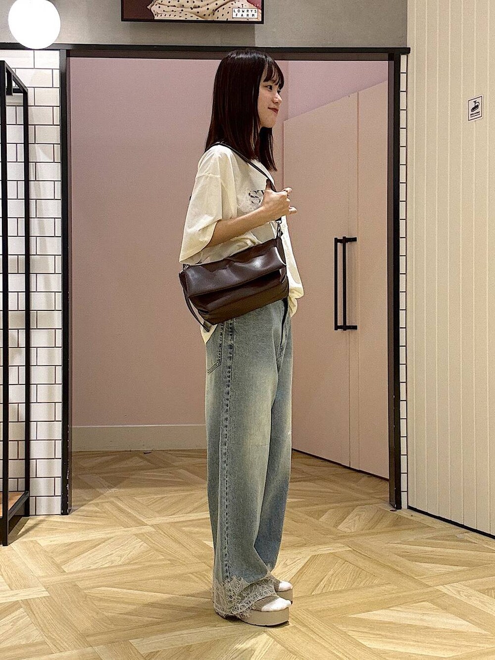 ブラウン系のショルダーバッグ、ベージュ系のTシャツ/カットソー、ブルー系のデニムパンツを着用したレディースの夏コーディネートの2枚目の写真