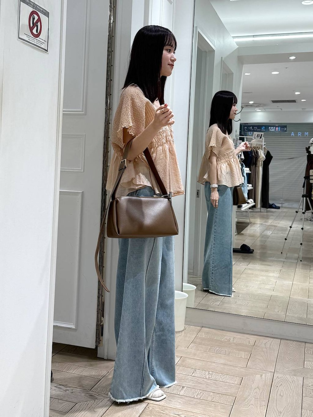 ブルー系のデニムパンツ、ブラウン系のショルダーバッグ、ホワイト系のサンダルを着用したレディースの春コーディネートの2枚目の写真