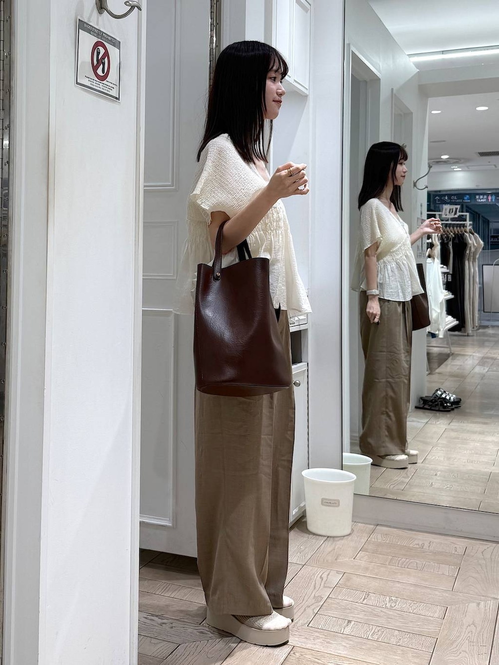 ベージュ系のスラックス、ホワイト系のサンダル、ブラウン系のトートバッグを着用したレディースの夏コーディネートの2枚目の写真