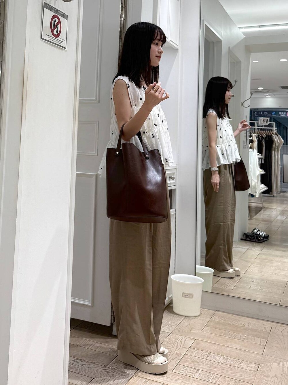 ベージュ系のスラックス、ホワイト系のサンダル、ブラウン系のトートバッグを着用したレディースの夏コーディネートの2枚目の写真