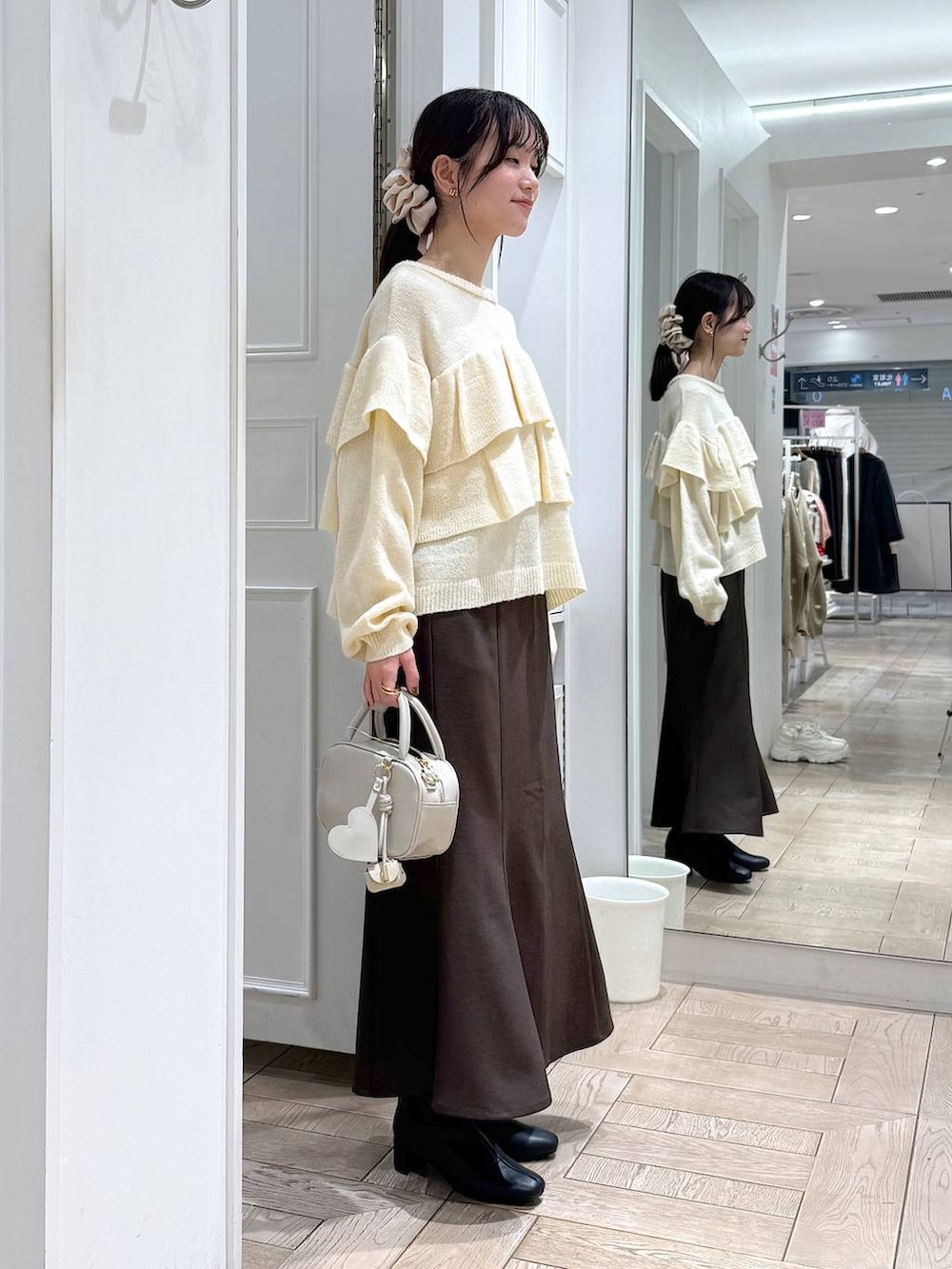 ブラウン系のスカート、ホワイト系のボストンバッグ、ブラック系のブーツを着用したレディースの冬コーディネートの2枚目の写真