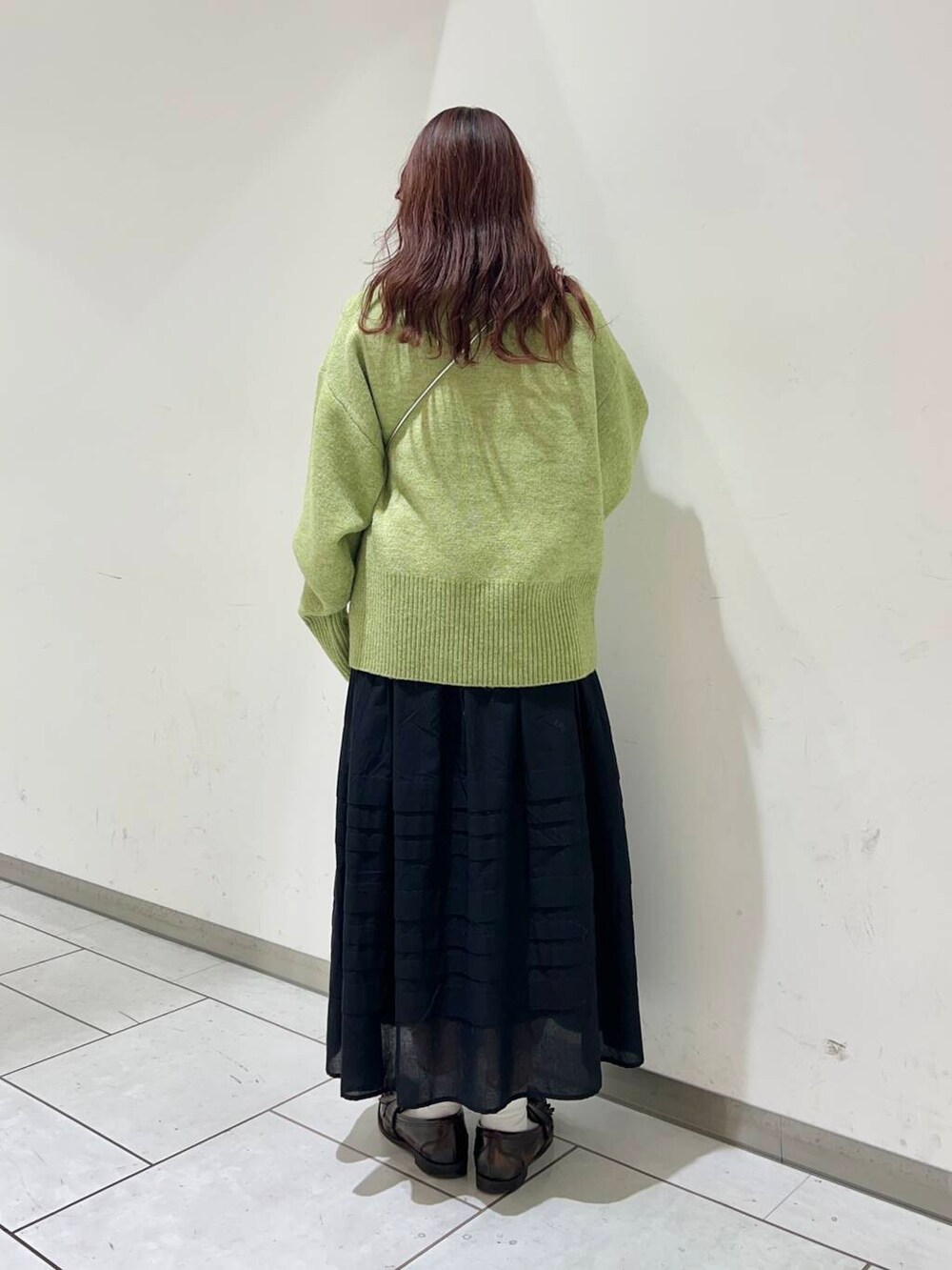 ブラック系のスカート、グリーン系のニット/セーター、シルバー系の財布を着用したレディースの冬コーディネートの2枚目の写真