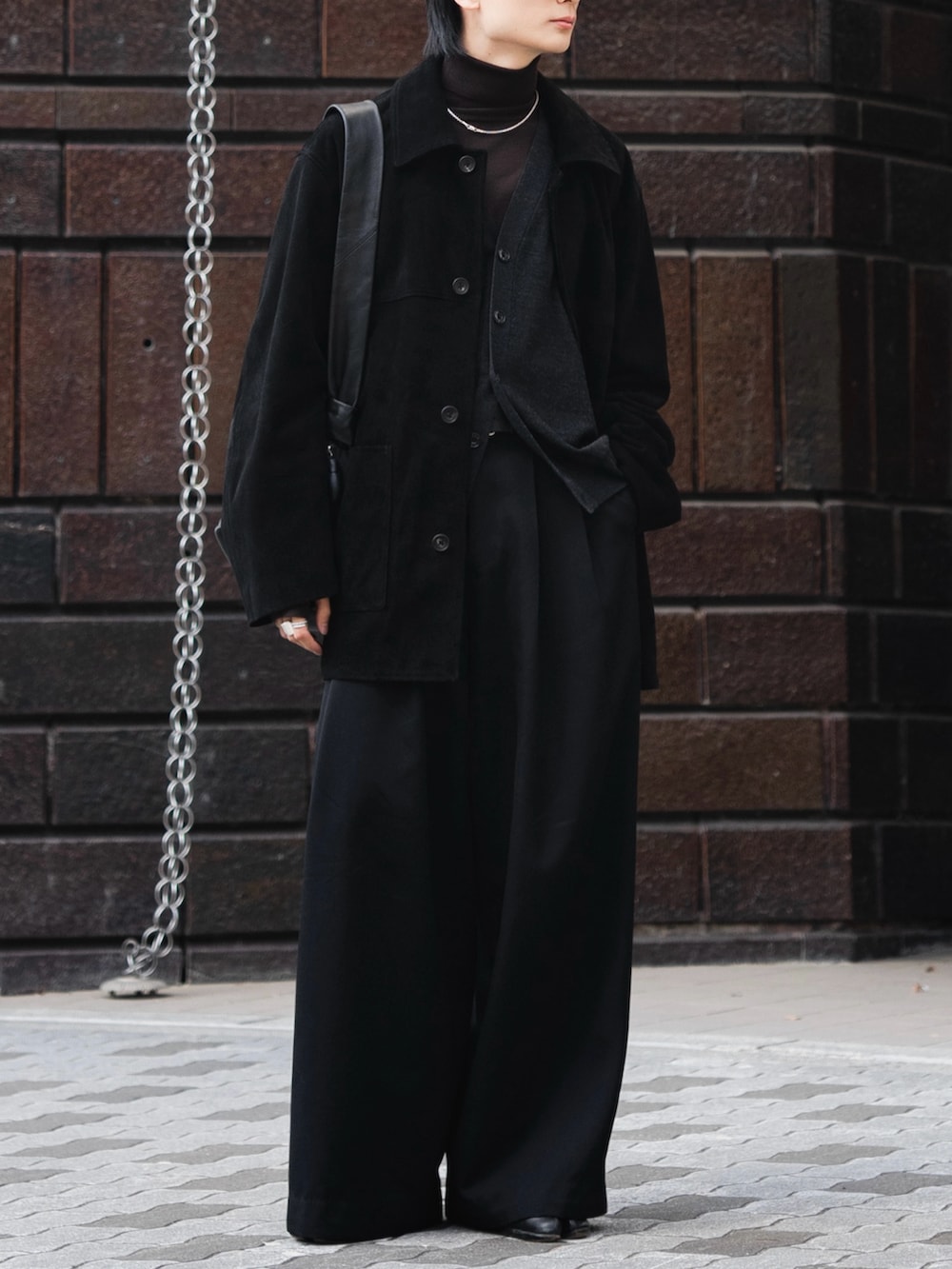 ブラック系のスラックス、ブラウン系のニット/セーター、ブラック系のショルダーバッグを着用したメンズの冬コーディネートの2枚目の写真