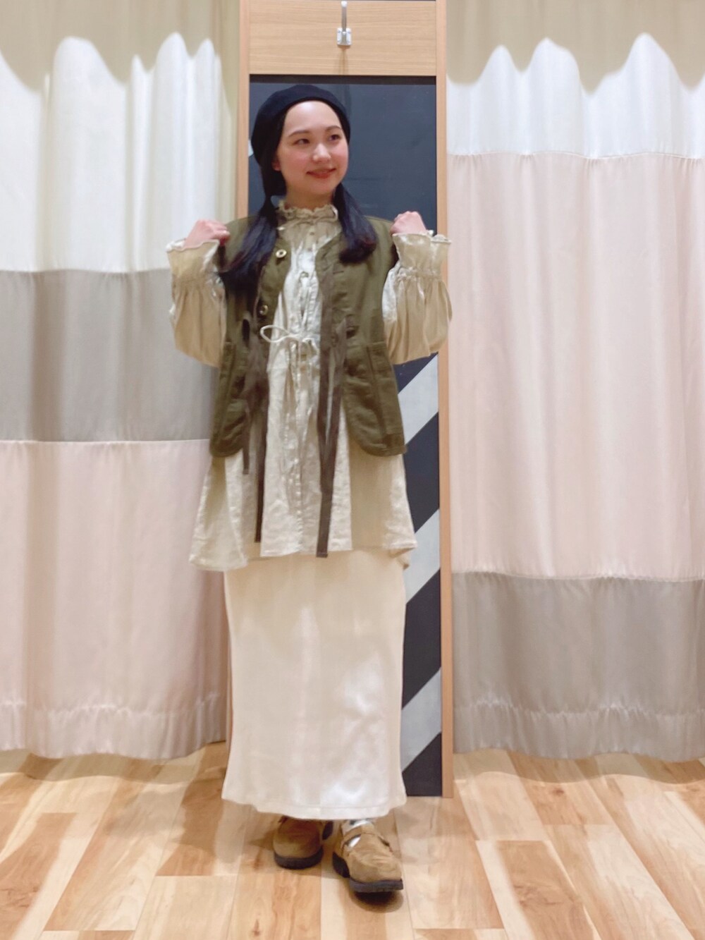 イエロー系のチュニック、グリーン系のベスト、ホワイト系のスカートを着用したレディースの春コーディネートの2枚目の写真