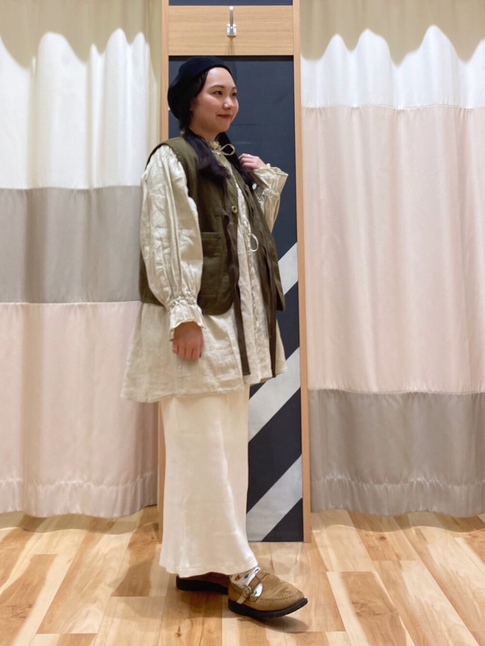 イエロー系のチュニック、グリーン系のベスト、ホワイト系のスカートを着用したレディースの春コーディネートの4枚目の写真