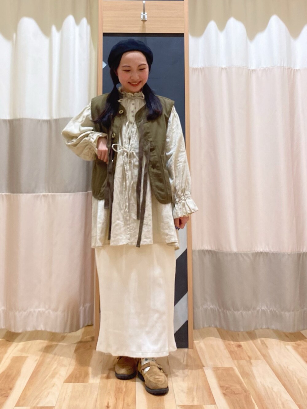 イエロー系のチュニック、グリーン系のベスト、ホワイト系のスカートを着用したレディースの春コーディネートの3枚目の写真