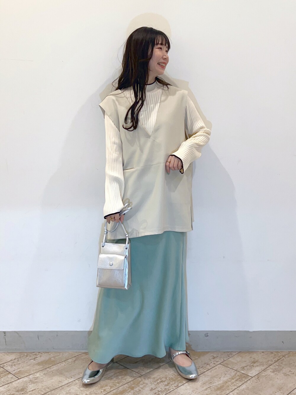 ホワイト系のベスト、グリーン系のスカート、シルバー系のパンプスを着用したレディースの春コーディネートの2枚目の写真