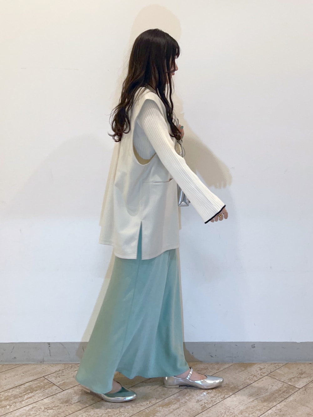 ホワイト系のベスト、グリーン系のスカート、シルバー系のパンプスを着用したレディースの春コーディネートの3枚目の写真