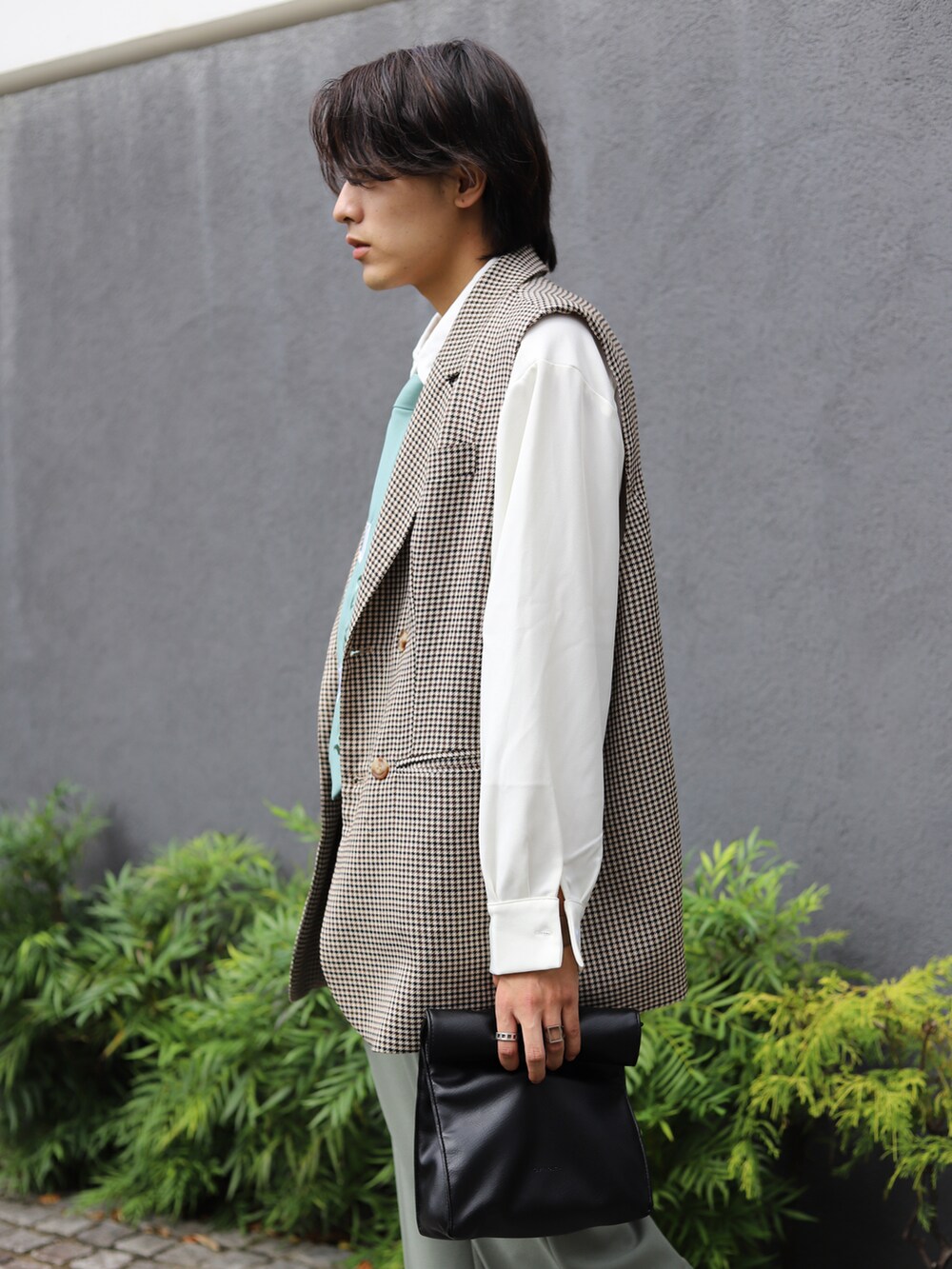 ブラウン系のベスト、ブルー系のスラックス、ブラック系のハンドバッグを着用したメンズの秋コーディネートの2枚目の写真