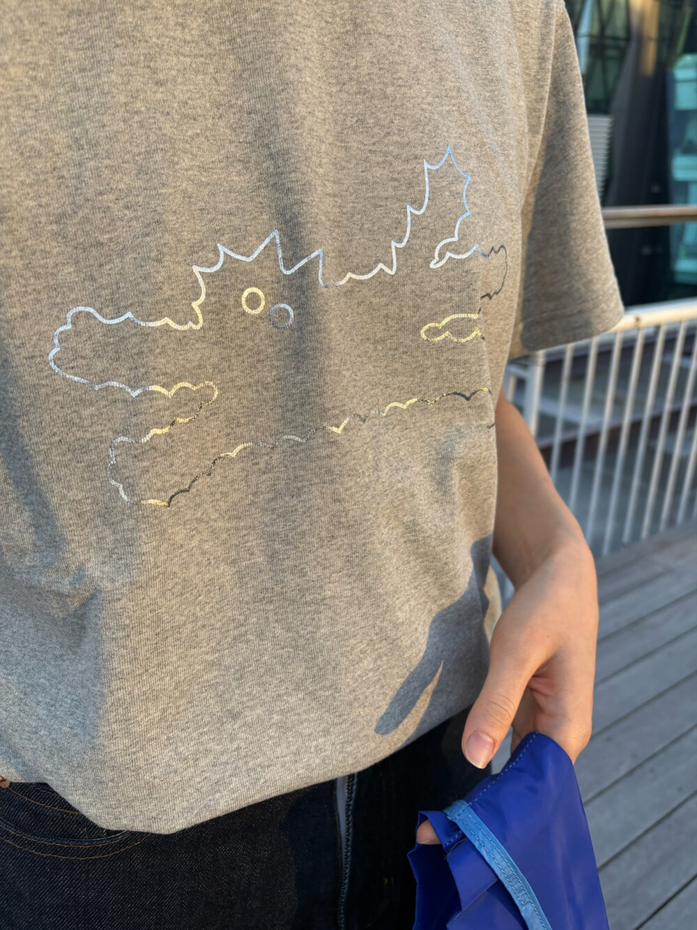 グレー系のTシャツ/カットソー、ブラック系のエコバッグ/サブバッグ、ブルー系のデニムパンツを着用したレディースの冬コーディネートの2枚目の写真