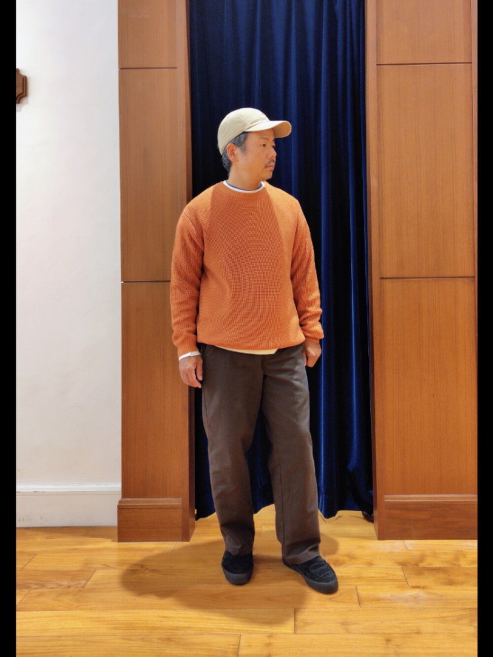 オレンジ系のニット/セーター、ベージュ系のキャップを着用したメンズの秋コーディネートの2枚目の写真