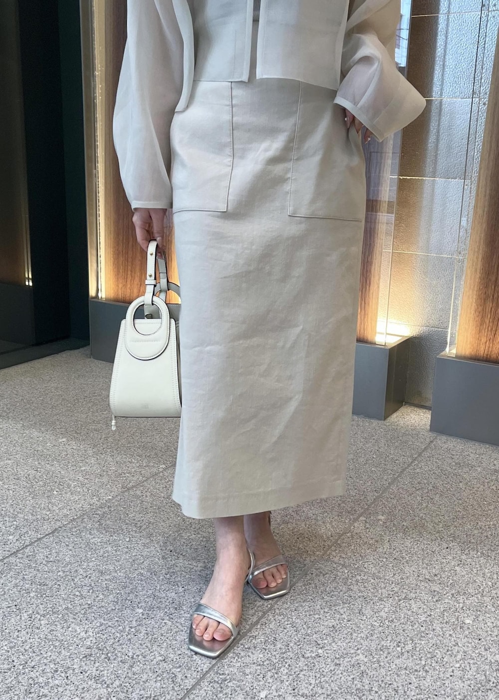 ホワイト系のハンドバッグ、シルバー系のサンダル、ベージュ系のスカートを着用したレディースの春コーディネートの9枚目の写真