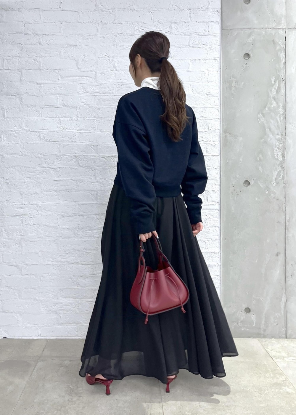 レッド系のパンプス、レッド系のハンドバッグ、ブラック系のスカートを着用したレディースの秋コーディネートの5枚目の写真