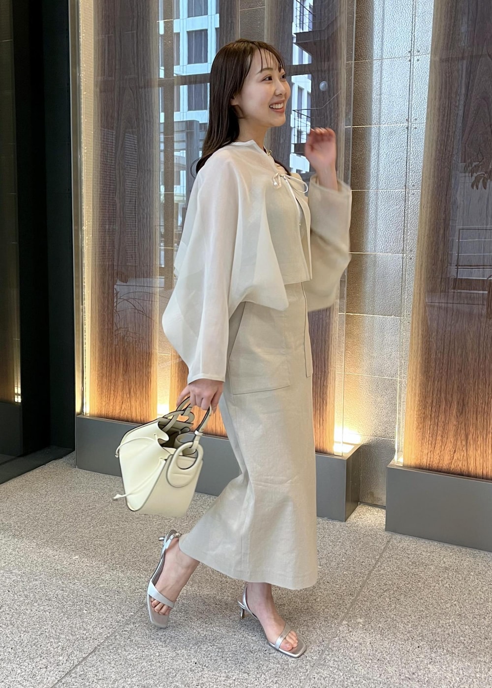 ホワイト系のハンドバッグ、シルバー系のサンダル、ベージュ系のスカートを着用したレディースの春コーディネートの2枚目の写真
