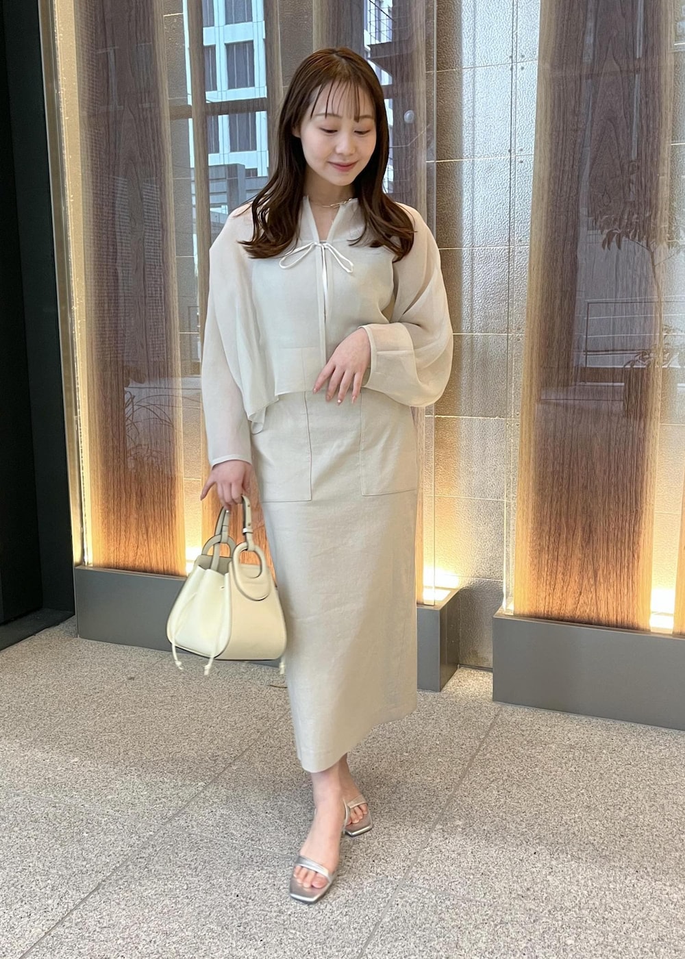 ホワイト系のハンドバッグ、シルバー系のサンダル、ベージュ系のスカートを着用したレディースの春コーディネートの6枚目の写真