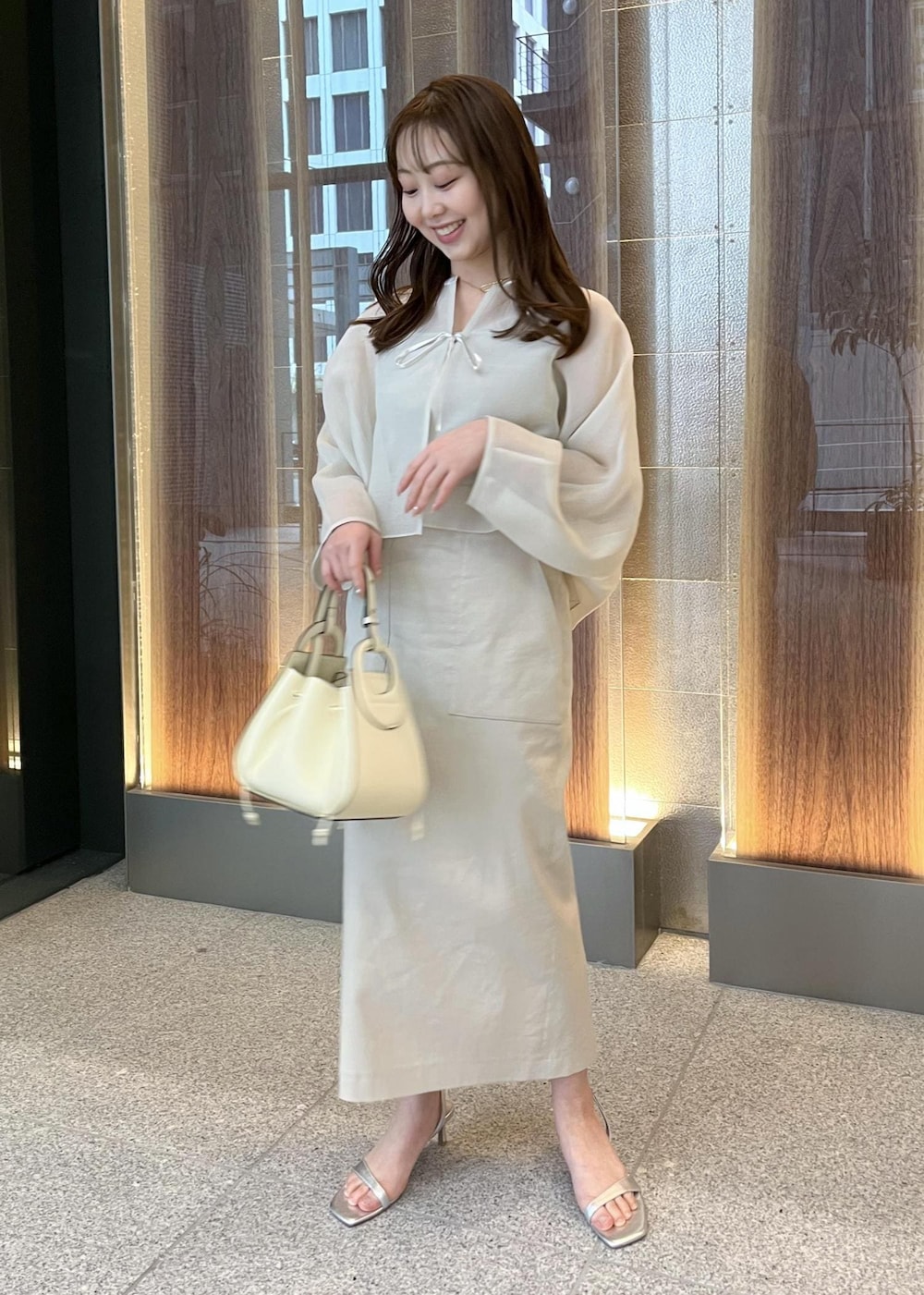 ホワイト系のハンドバッグ、シルバー系のサンダル、ベージュ系のスカートを着用したレディースの春コーディネートの4枚目の写真