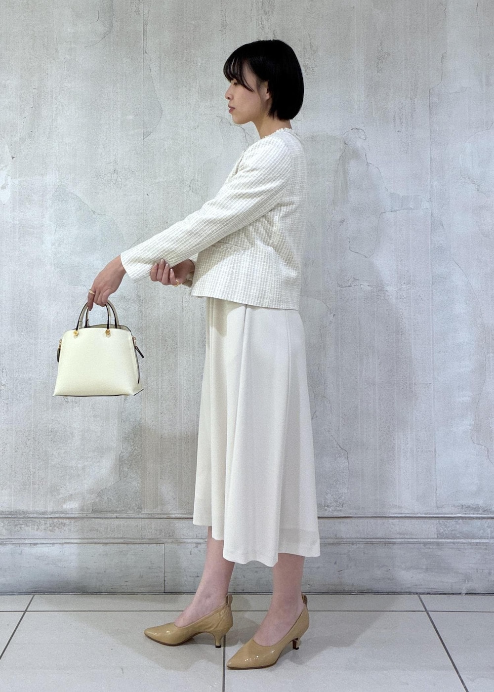 ベージュ系のワンピース、ホワイト系のノーカラージャケット、ホワイト系のハンドバッグを着用したレディースの冬コーディネートの3枚目の写真