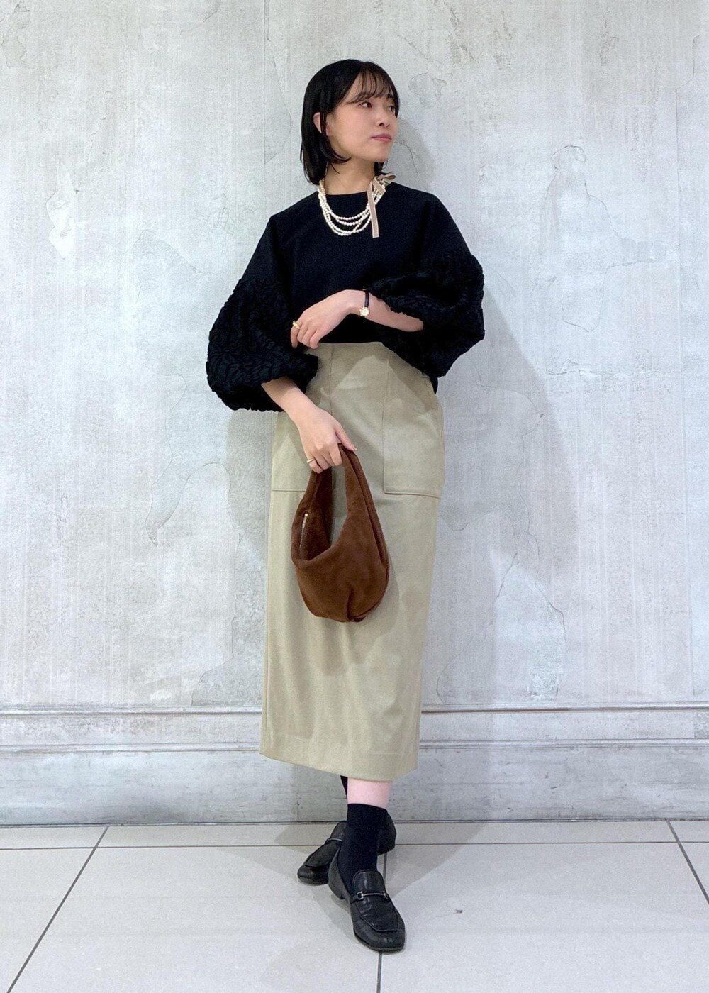 ブラウン系のハンドバッグ、ベージュ系のスカート、ブラック系のシャツ/ブラウスを着用したレディースの冬コーディネートの6枚目の写真