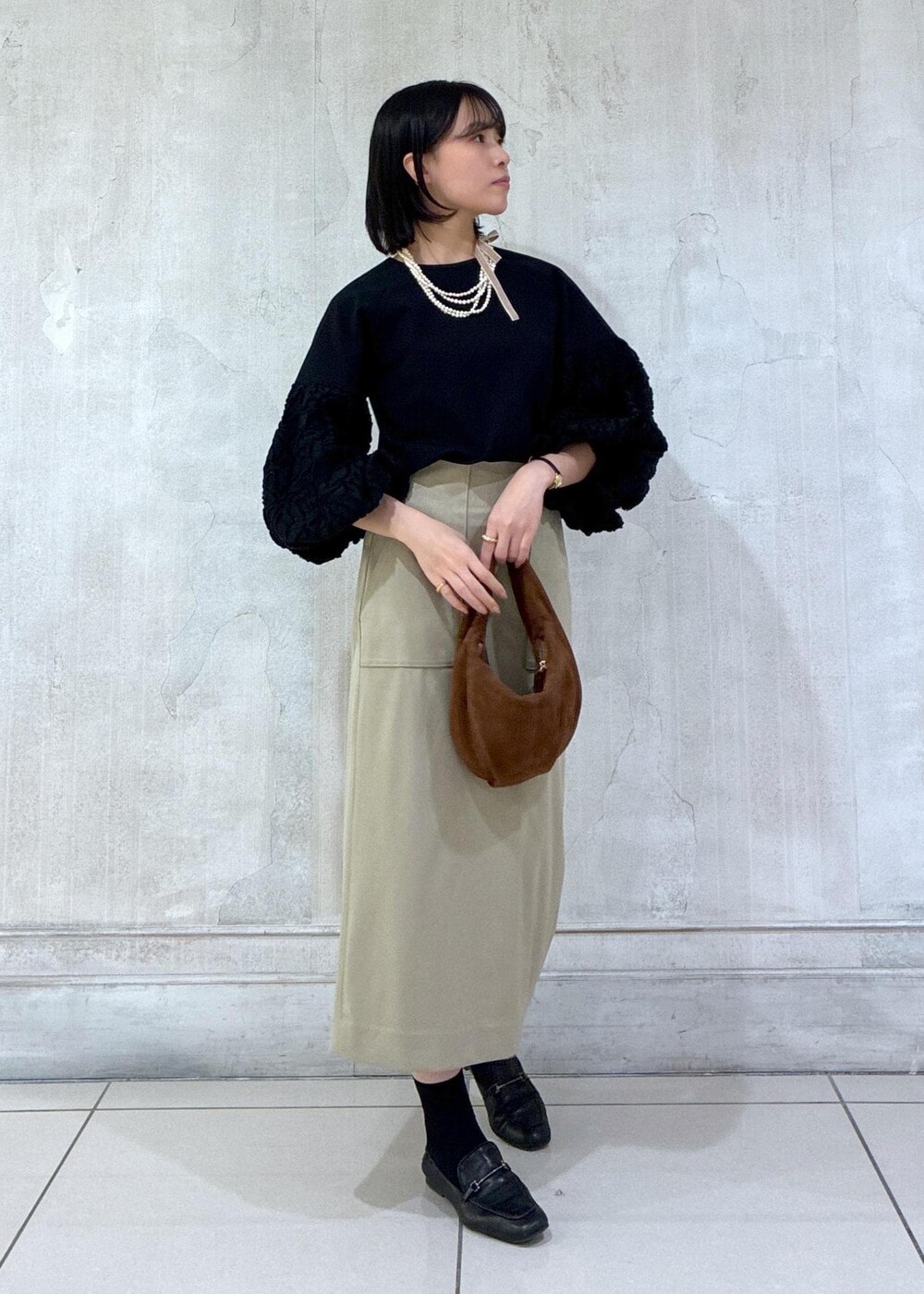 ブラウン系のハンドバッグ、ベージュ系のスカート、ブラック系のシャツ/ブラウスを着用したレディースの冬コーディネートの2枚目の写真
