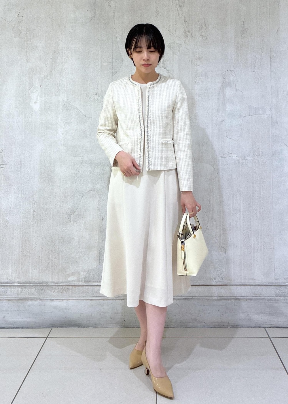 ベージュ系のワンピース、ホワイト系のノーカラージャケット、ホワイト系のハンドバッグを着用したレディースの冬コーディネートの2枚目の写真