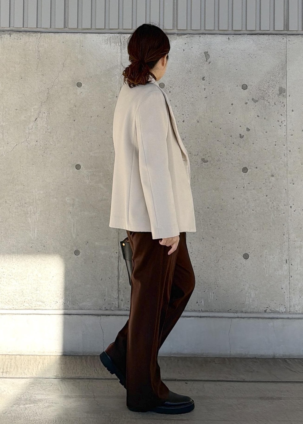 ブラック系のハンドバッグ、ホワイト系のステンカラーコート、ブラウン系のニット/セーターを着用したレディースの冬コーディネートの2枚目の写真