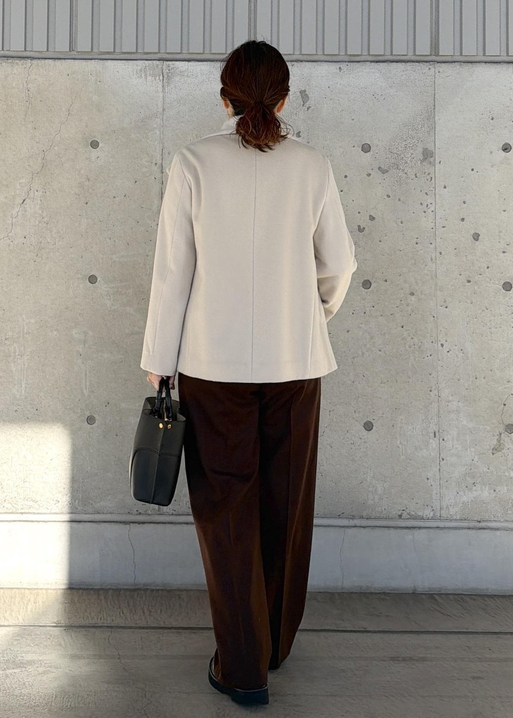 ブラック系のハンドバッグ、ホワイト系のステンカラーコート、ブラウン系のニット/セーターを着用したレディースの冬コーディネートの3枚目の写真