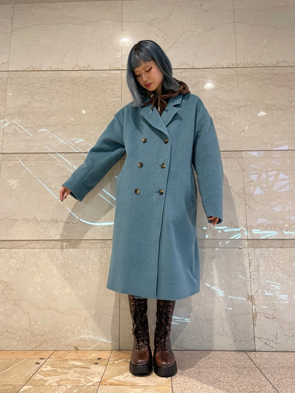 ブルー系のチェスターコート、ブラウン系のパーカー、ブラウン系のブーツを着用したレディースの冬コーディネートの2枚目の写真