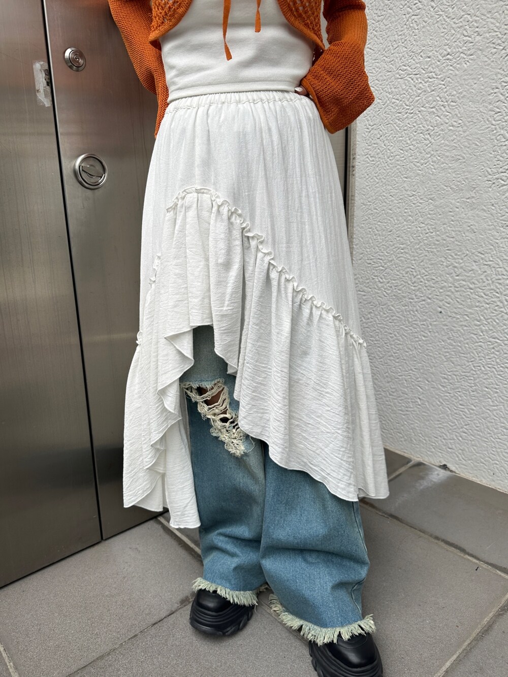 オレンジ系のカーディガン/ボレロ、ホワイト系のスカート、ブルー系のデニムパンツを着用したレディースの冬コーディネートの8枚目の写真