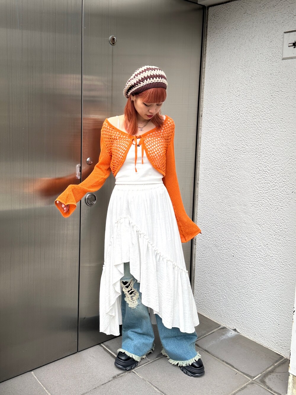 オレンジ系のカーディガン/ボレロ、ホワイト系のスカート、ブルー系のデニムパンツを着用したレディースの冬コーディネートの4枚目の写真