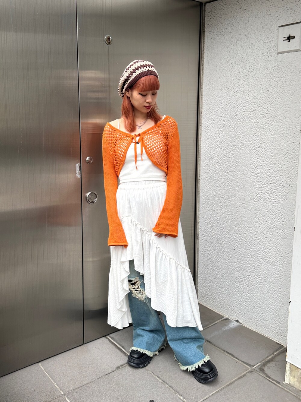 オレンジ系のカーディガン/ボレロ、ホワイト系のスカート、ブルー系のデニムパンツを着用したレディースの冬コーディネートの2枚目の写真