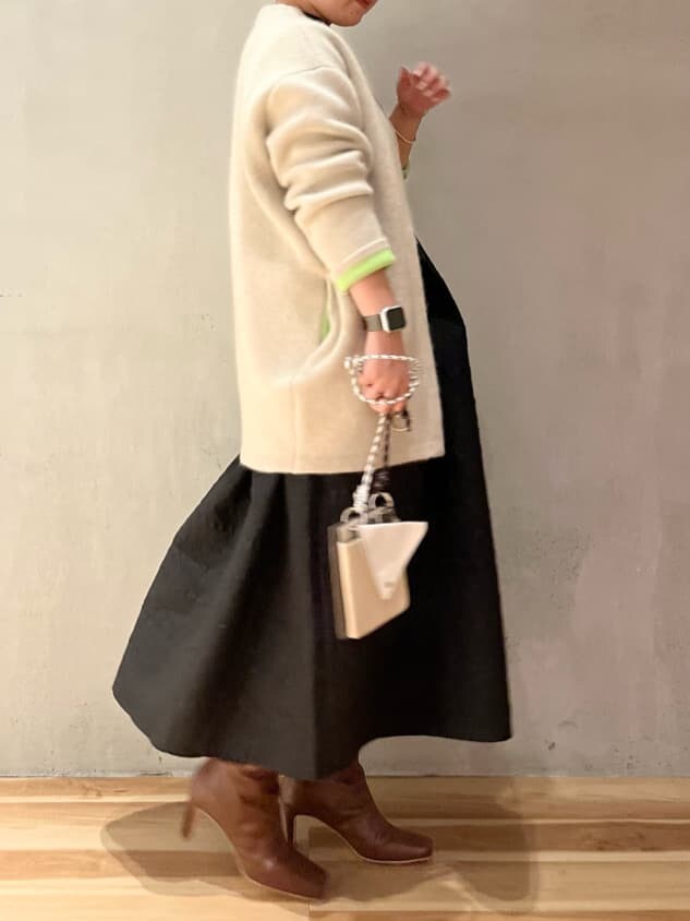 ベージュ系のショルダーバッグ、ホワイト系のカーディガン/ボレロ、ブラウン系のブーツを着用したレディースの秋コーディネートの2枚目の写真