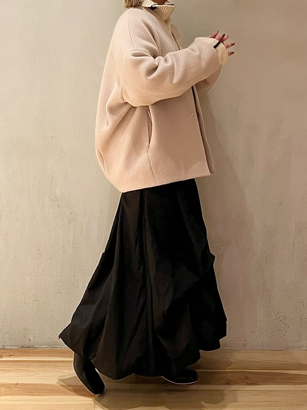 ベージュ系のノーカラーコート、ブラック系のスカート、ブラック系のブーツを着用したレディースの夏コーディネートの2枚目の写真