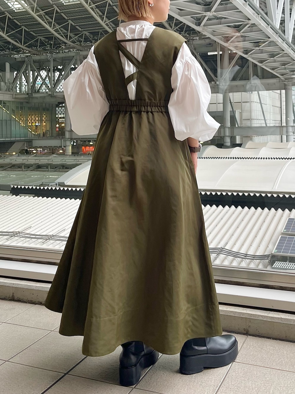 ホワイト系のシャツ/ブラウス、グリーン系のジャンパースカート、ブラック系のブーツを着用したレディースの春コーディネートの2枚目の写真