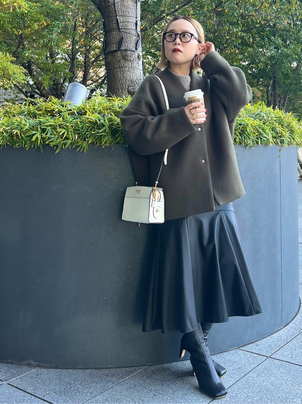ブラック系のスカート、ブラック系のブーツ、グリーン系のノーカラーコートを着用したレディースの秋コーディネートの4枚目の写真