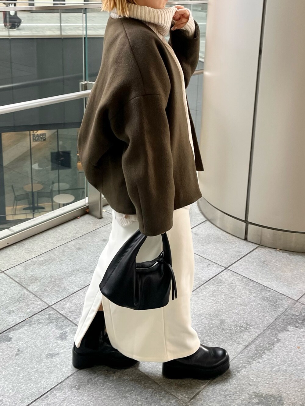 グリーン系のノーカラーコート、ブラック系のブーツを着用したレディースの冬コーディネートの4枚目の写真